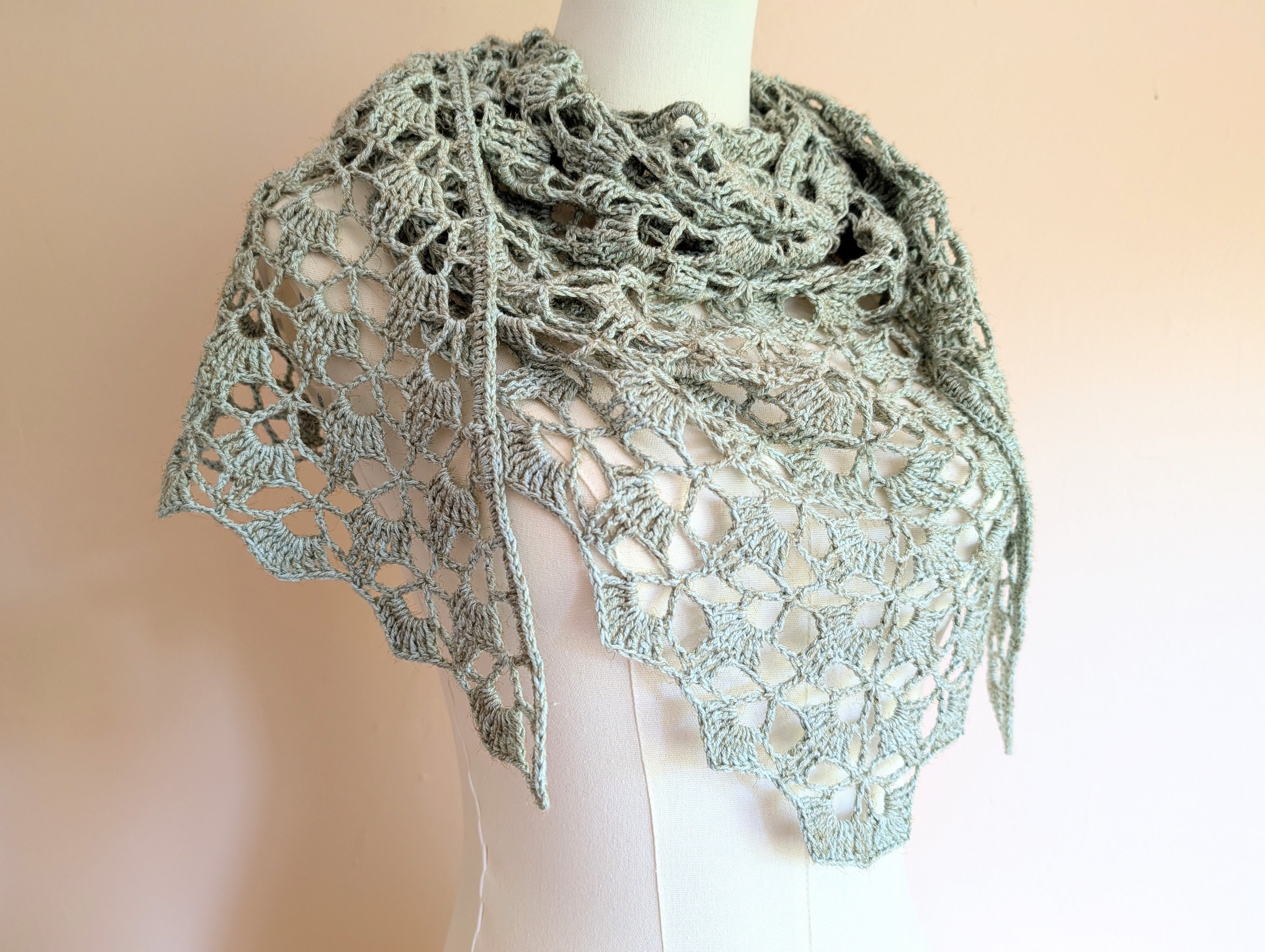 Crocheted triangle neck scarf in sage green cotton-viscose yarn with open lace stitch pattern, draped on a dress form - Chart #10 by Simply Crochet Charts