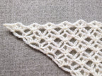 Close-up shot of intricate lace stitches and openwork mesh texture on a crochet bandana shawl.