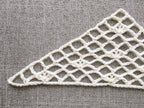 Close-up shot of intricate lace stitches and openwork mesh texture on a crochet bandana shawl.