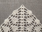 Close-up shot of intricate lace stitches and openwork mesh texture on a crochet bandana shawl.