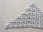 Close-up shot of intricate lace stitches and openwork mesh texture on a crochet bandana shawl.