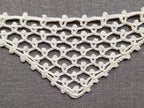 Close-up shot of intricate lace stitches and openwork mesh texture on a crochet bandana shawl.