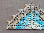 Close-up shot of intricate lace stitches and openwork mesh texture on a crochet bandana shawl.