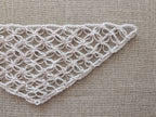 Close-up shot of intricate lace stitches and openwork mesh texture on a crochet bandana shawl.