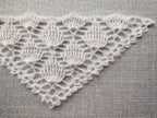 Close-up shot of intricate lace stitches and openwork mesh texture on a crochet bandana shawl.