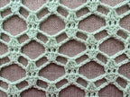 Close-up shot of intricate lace stitches and openwork mesh texture on a crochet scarf.