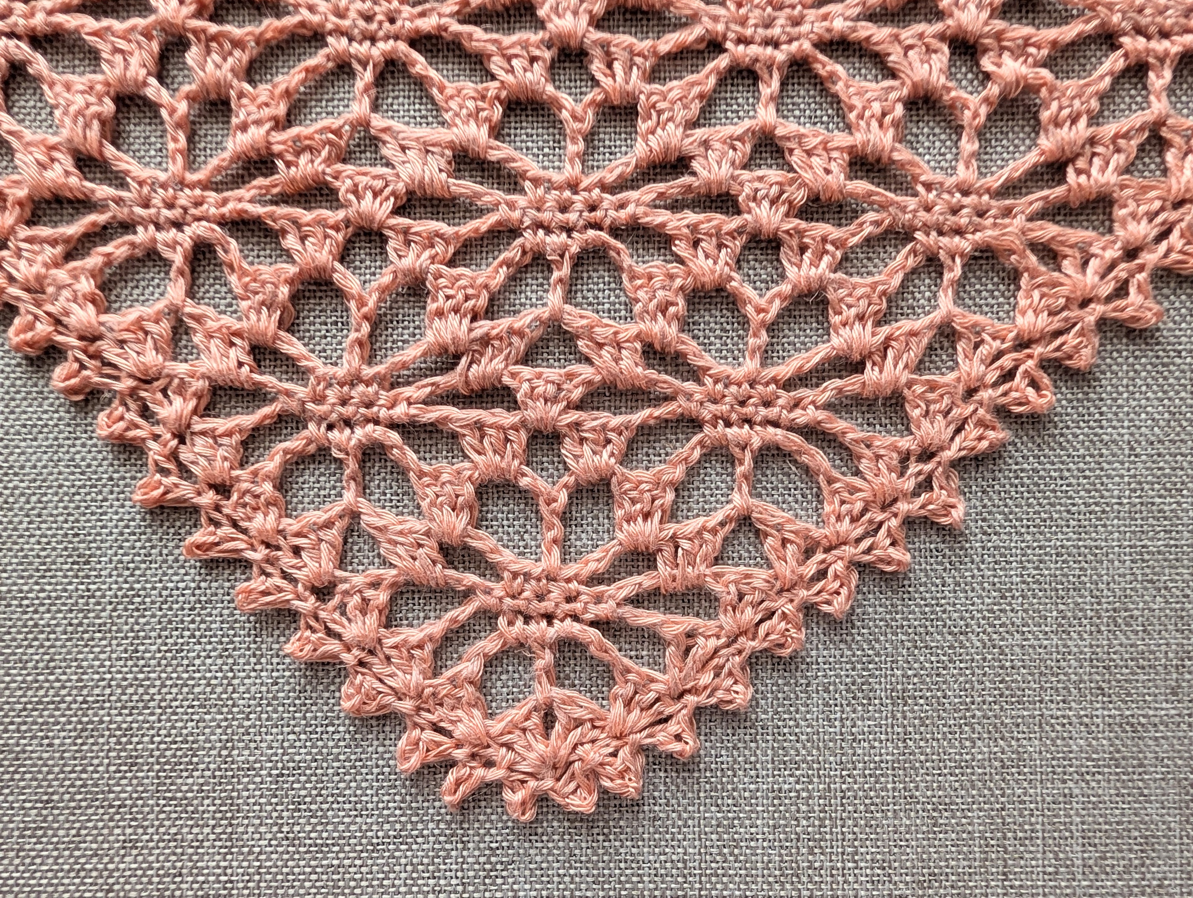 Detailed view of intricate lace pattern and decorative edge on dusty pink crochet kerchief.